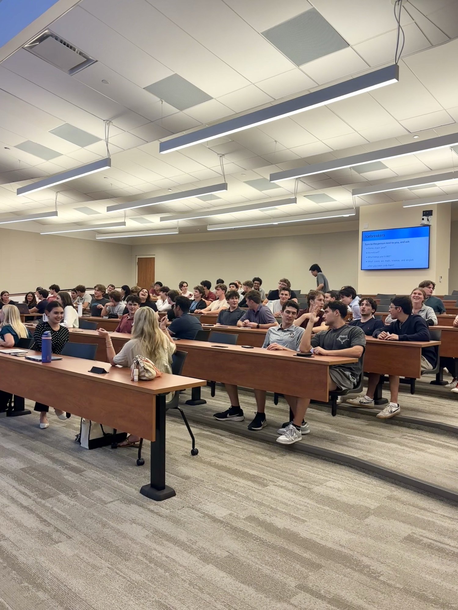 Workshop attendees seated in a lecture room, talking with one another.